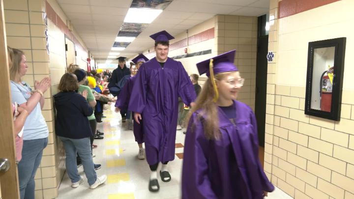 High School seniors in cap and grown in hallway with cheering elementary students.
